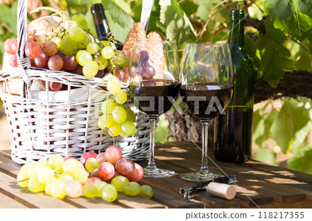 Red wine ripe grapes and picnic basket on table in vineyard 118217355