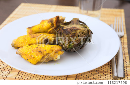 Cooked fried chicken wings and halves artichokes on white plate 118217398