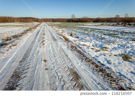 Little snow and ice on the dirt road through the rural fields 118218507