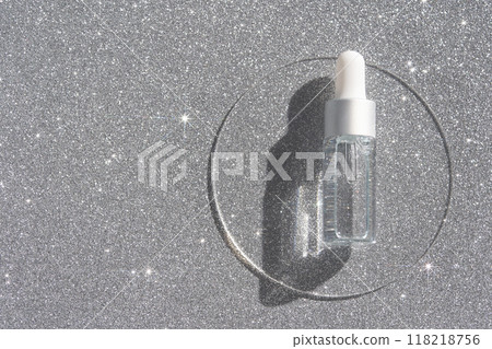 Transparent serum bottle with dropper on sparkling silver surface highlighting Transparent serum bottle with dropper on sparkling silver surface highlighting 118218756