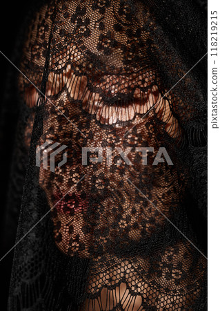 Close up of woman with eyes closed wearing black mourning veil made of delicate lace covering face in studio 118219215