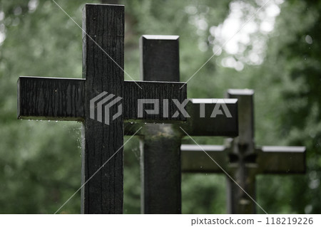 Background shot of granite memorial crosses wet from rain standing in row on graves in shades of old cemetery trees commemorating deceased people, copy space Background shot of granite memorial crosses wet from rain standing in row on graves in shades of old cemetery trees commemorating deceased people, copy space 118219226