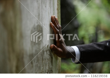 Close up on hand of Black man grieving over loss of loved one touching weathered memorial monument covered moss at grave at cemetery, copy space Close up on hand of Black man grieving over loss of loved one touching weathered memorial monument covered moss at grave at cemetery, copy space 118219338