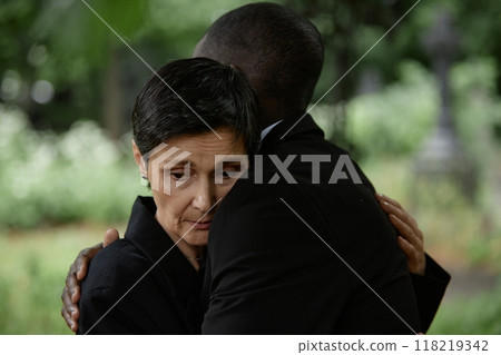 Portrait shot of sorrowful senior woman comforting husband with embrace grieving over loss of loved one during memorial ceremony at graveyard, copy space 118219342