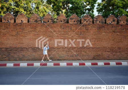 A woman is walking down a street in front of a brick wall A woman is walking down a street in front of a brick wall 118219578