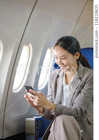 A woman is sitting on an airplane and looking at her cell phone 118219635