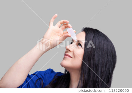 Woman applying eye drops for eye care and relief against gray background Woman applying eye drops for eye care and relief against gray background 118220090