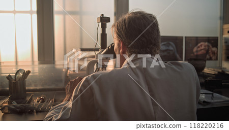Mature microbiologist analyzes fossil sample under microscope 118220216