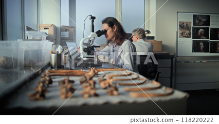 Female scientist analyzes sample of fossil remains under microscope 118220222