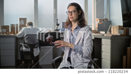Female lab worker speaks, shows 3D visualization of human head on tablet during interview 118220234
