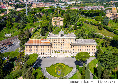 The Governorates Palace in Vatican is showcased from above, featuring its stunning architecture surrounded by meticulously manicured gardens and lush greenery, set against the city's backdrop. 118220573