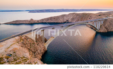 Pag Bridge with driving vehicles over Adriatic Sea channel at sunset. Road network connects island to Croatian mainland offering stunning views Pag Bridge with driving vehicles over Adriatic Sea channel at sunset. Road network connects island to Croatian mainland offering stunning views 118220614