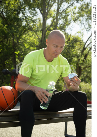 Basketball player eating energy bar or protein bar while resting after training at stadium. Healthy protein sugar free snack dieting food for sporty lifestyle. Basketball player eating energy bar or protein bar while resting after training at stadium. Healthy protein sugar free snack dieting food for sporty lifestyle. 118222125