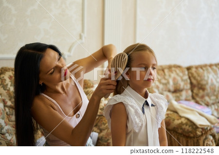 Mother brushing daughters hair in a cozy living room on a sunny morning Mother brushing daughters hair in a cozy living room on a sunny morning 118222548