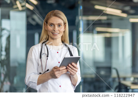Confident female doctor with stethoscope using tablet in modern office. Smiling medical professional providing healthcare consultation and innovative solutions. 118222947