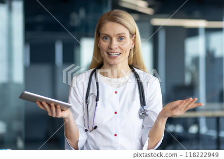Smiling female doctor with stethoscope using tablet for online consultation. Confident professional in white coat communicating through video call in modern office. Medical technology concept. Smiling female doctor with stethoscope using tablet for online consultation. Confident professional in white coat communicating through video call in modern office. Medical technology concept. 118222949