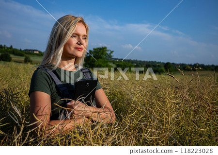 A woman farmer standing in the middle of rapeseed field, holding a tablet close to her body and satysfied with her rapeseed crop A woman farmer standing in the middle of rapeseed field, holding a tablet close to her body and satysfied with her rapeseed crop 118223028