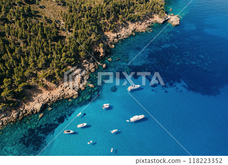 Aerial view of a secluded cove with clear turquoise waters, surrounded by rocky cliffs and boats anchored near the shore Aerial view of a secluded cove with clear turquoise waters, surrounded by rocky cliffs and boats anchored near the shore 118223352
