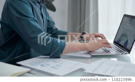 Entrepreneur wearing green shirt is working at laptop with data analysis charts. Businessman analyzing statistical data. Business concept 118223996