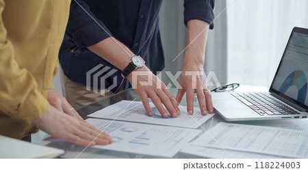 Business people, professionals analyzing financial charts and data on a desk while standing and using laptop computer in office. Dark blue shirt and yellow blouse 118224003