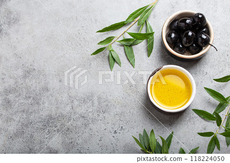 Black olives and extra virgin olive oil in little bowl with olive tree branches top view on grey concrete stone background, space for text 118224050