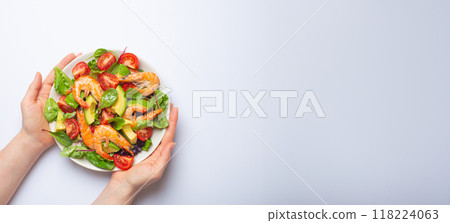 Female hands holding salad with grilled shrimps, avocado, vegetables, green leaves on white plate isolated on white background top view. Clean eating, nutrition and dieting concept, copy space. Female hands holding salad with grilled shrimps, avocado, vegetables, green leaves on white plate isolated on white background top view. Clean eating, nutrition and dieting concept, copy space. 118224063