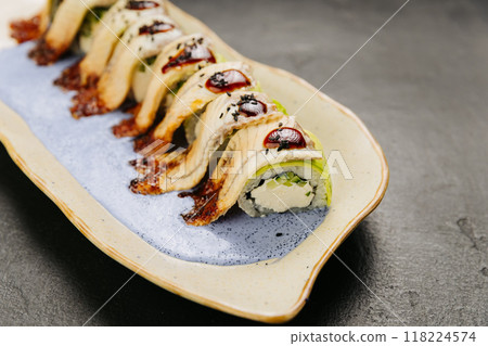 Eel sushi roll with creamy filling, topped with savory sauce and sesame seeds on a stylish plate 118224574