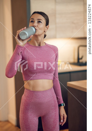 Fit woman dressed in sportswear drinking bottle of mineral water after her fitness training session 118224874