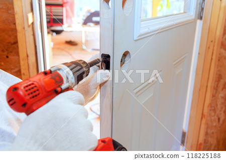 An experienced locksmith installs lock doorknob on entrance door of home using screwdriver An experienced locksmith installs lock doorknob on entrance door of home using screwdriver 118225188