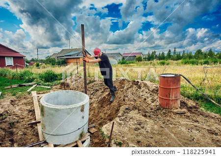 Builder places one concrete ring on top of another and levels it with lever using steel pipe when building septic tank. 118225941