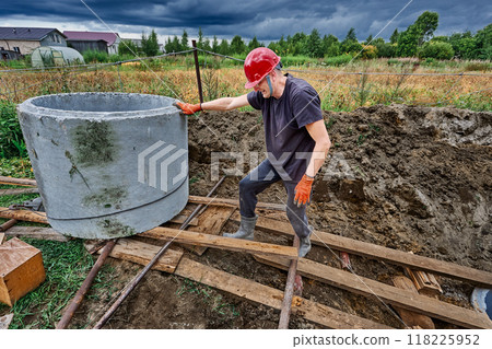 Construction worker uses winch to move concrete ring along sloping wooden deck during installation of septic tank. Construction worker uses winch to move concrete ring along sloping wooden deck during installation of septic tank. 118225952