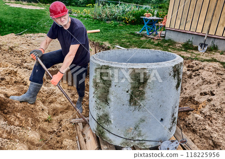 When building septic tank in rural area, worker moves concrete ring using crowbar as lever. 118225956