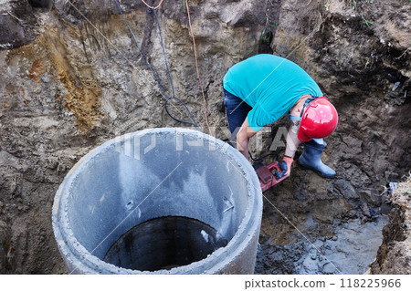 Construction worker is chiseling big hole in concrete ring with rotary hammer. 118225966