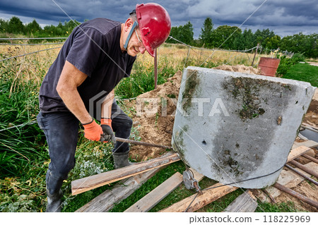 Builder uses crowbar to move concrete ring along rollers while installing septic tank. 118225969