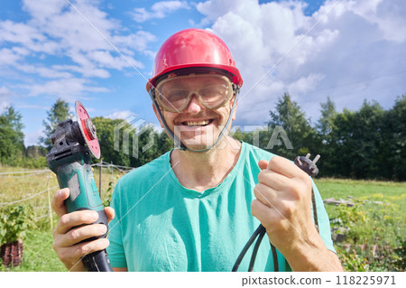 Smiling worker in construction helmet, safety glasses and an angle grinder in his hands. Smiling worker in construction helmet, safety glasses and an angle grinder in his hands. 118225971
