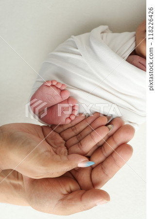 The palms of the parents. A father and mother hold the feet of a newborn child in a white blanket on a white background.. The feet of a newborn in the hands of parents. Photo of foot, heels and toes The palms of the parents. A father and mother hold the feet of a newborn child in a white blanket on a white background.. The feet of a newborn in the hands of parents. Photo of foot, heels and toes 118226426