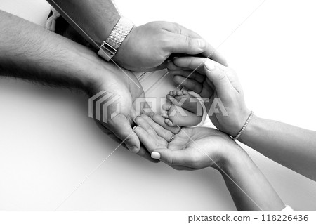 The palms of the parents. A father and mother hold the feet of a newborn child in a blanket. The feet of a newborn in the hands of parents. Black and white Photo of foot, heels and toes 118226436