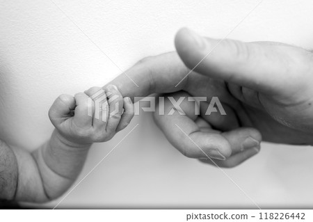 The newborn baby has a firm grip on the parent's finger after birth. Close-up little hand of child and palm of mother and father. Parenting, childcare and healthcare concept. Black and white photo. The newborn baby has a firm grip on the parent's finger after birth. Close-up little hand of child and palm of mother and father. Parenting, childcare and healthcare concept. Black and white photo. 118226442