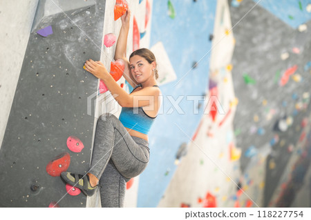 Young girl climbing on artificial rock wall in rock-climbing gym Young girl climbing on artificial rock wall in rock-climbing gym 118227754