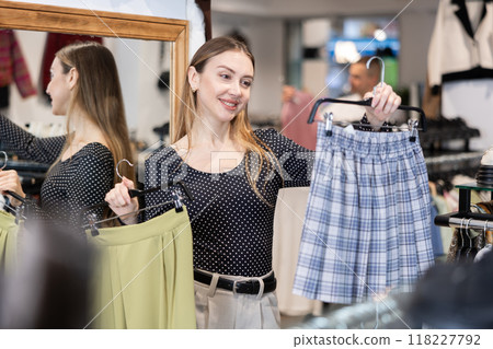 Girl stopped near showcase with outerwear, holds skirt hanger in hands and examines product 118227792