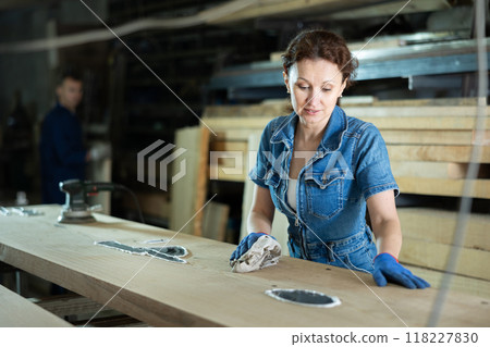 Adult woman wipes oak plank in workshop 118227830