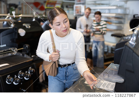 In store, girl inspects mobile grill, buys barbecue device In store, girl inspects mobile grill, buys barbecue device 118227867