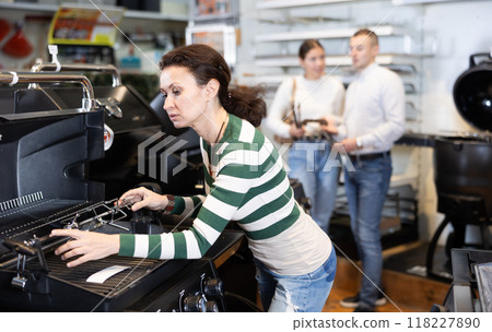 In store, woman inspects mobile grill, buys barbecue device In store, woman inspects mobile grill, buys barbecue device 118227890