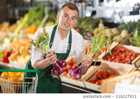 Male seller displaying bunches of purple onions at farmers market 118227911