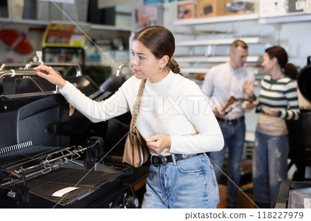 In store, girl inspects mobile grill, buys barbecue device In store, girl inspects mobile grill, buys barbecue device 118227979