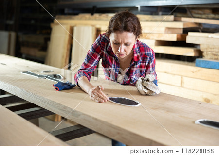 Adult woman wipes oak plank in workshop 118228038