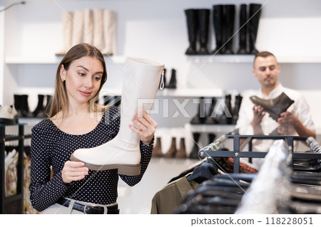 Girl buyer looks at footwear from new collection and picks up new pair of high boot Girl buyer looks at footwear from new collection and picks up new pair of high boot 118228051
