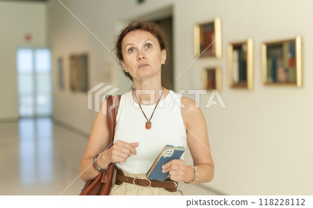 Young woman visitor enjoying works of art, holding and using phone in museum Young woman visitor enjoying works of art, holding and using phone in museum 118228112