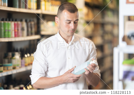 Thoughtful young man purchaser choosing cosmetic product in large supermarket Thoughtful young man purchaser choosing cosmetic product in large supermarket 118228113