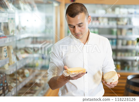Man in bio food store holds cheese of different varieties in hands and is thinking about buying Man in bio food store holds cheese of different varieties in hands and is thinking about buying 118228126